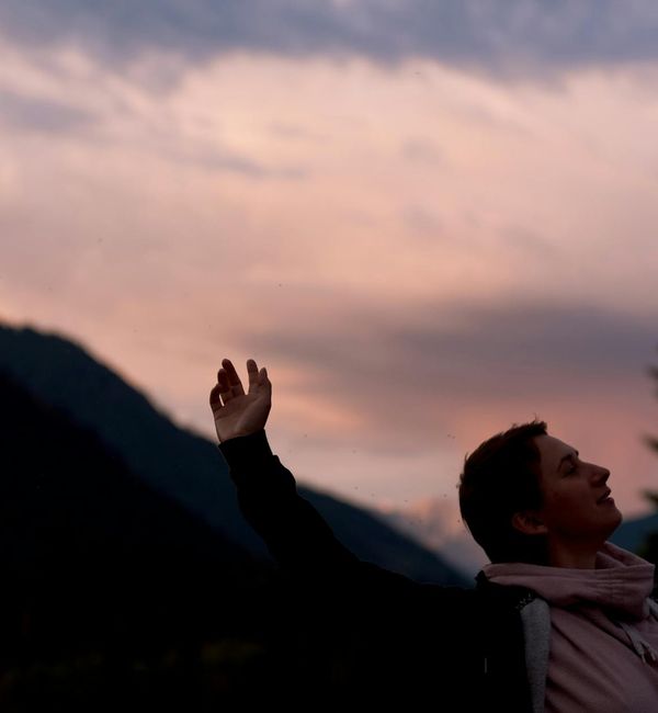 Person meditating peacefully outdoors during a sunset with pink sky.